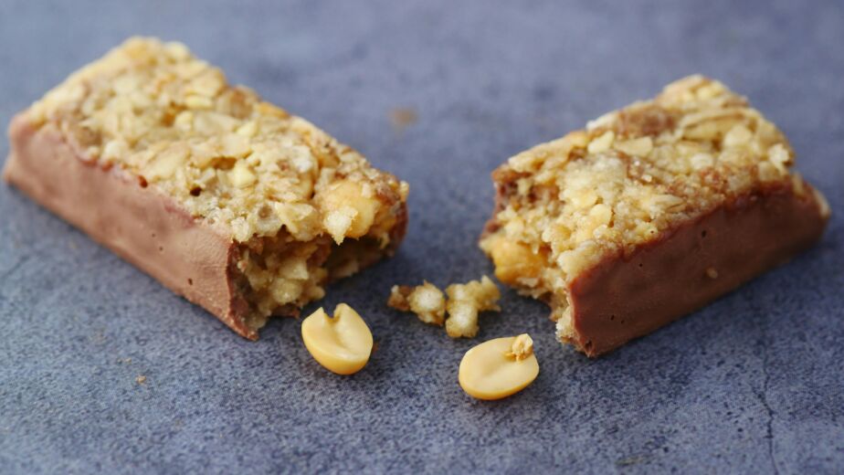 Close-up of a broken chocolate and nut energy bar on a gray surface.