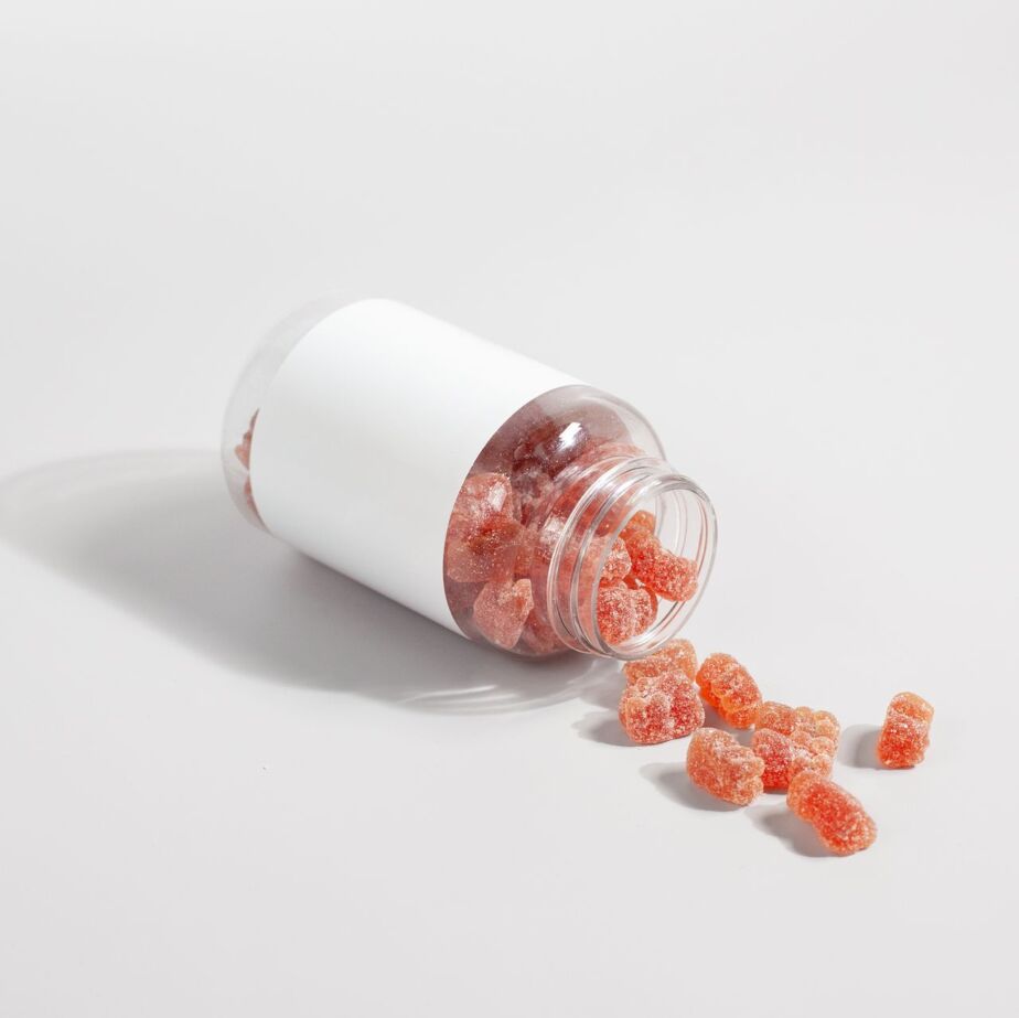 Close-up of gummy vitamins spilled from a clear bottle on a white surface