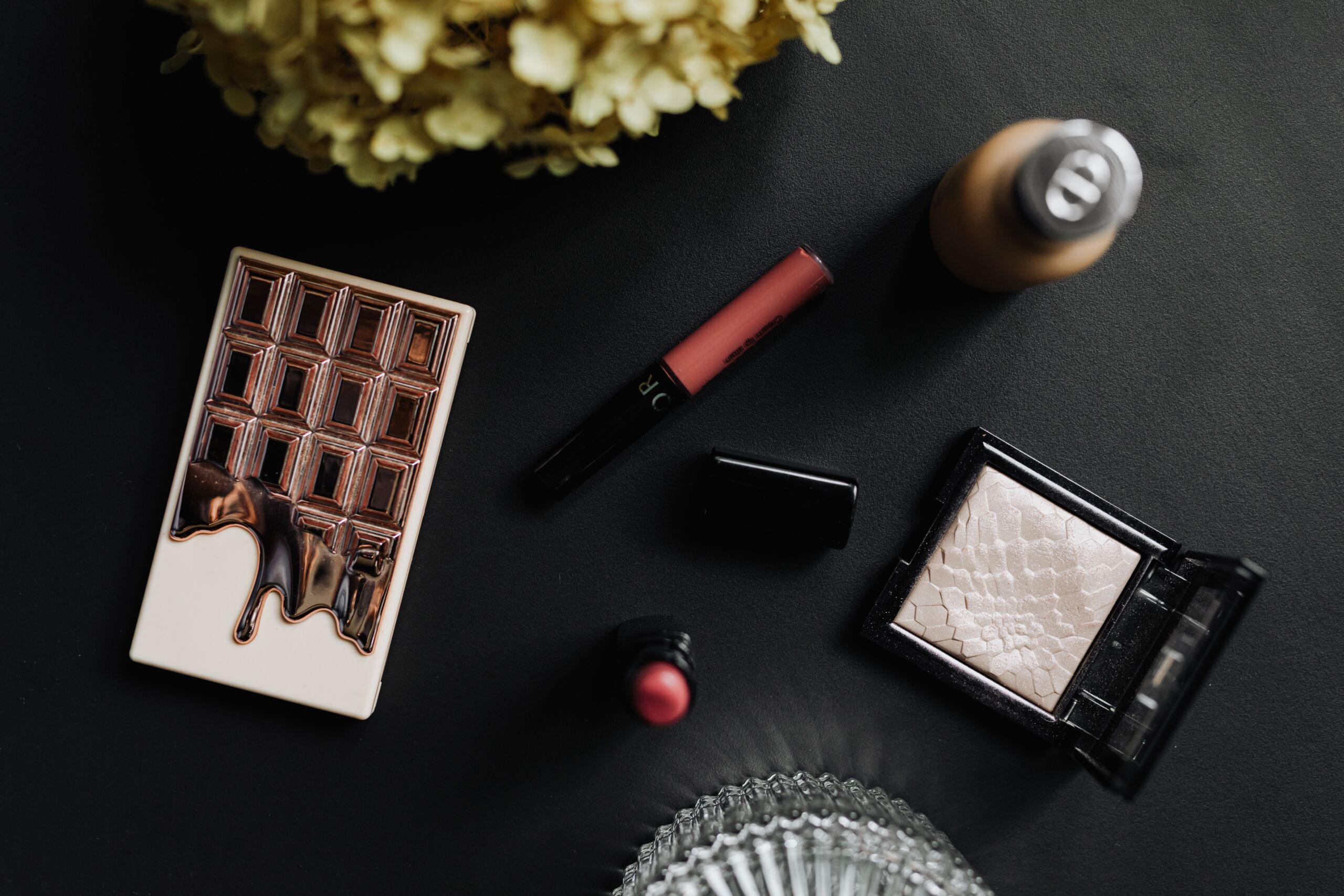 Flat lay of luxury makeup items on a black table with cosmetics and accessories.