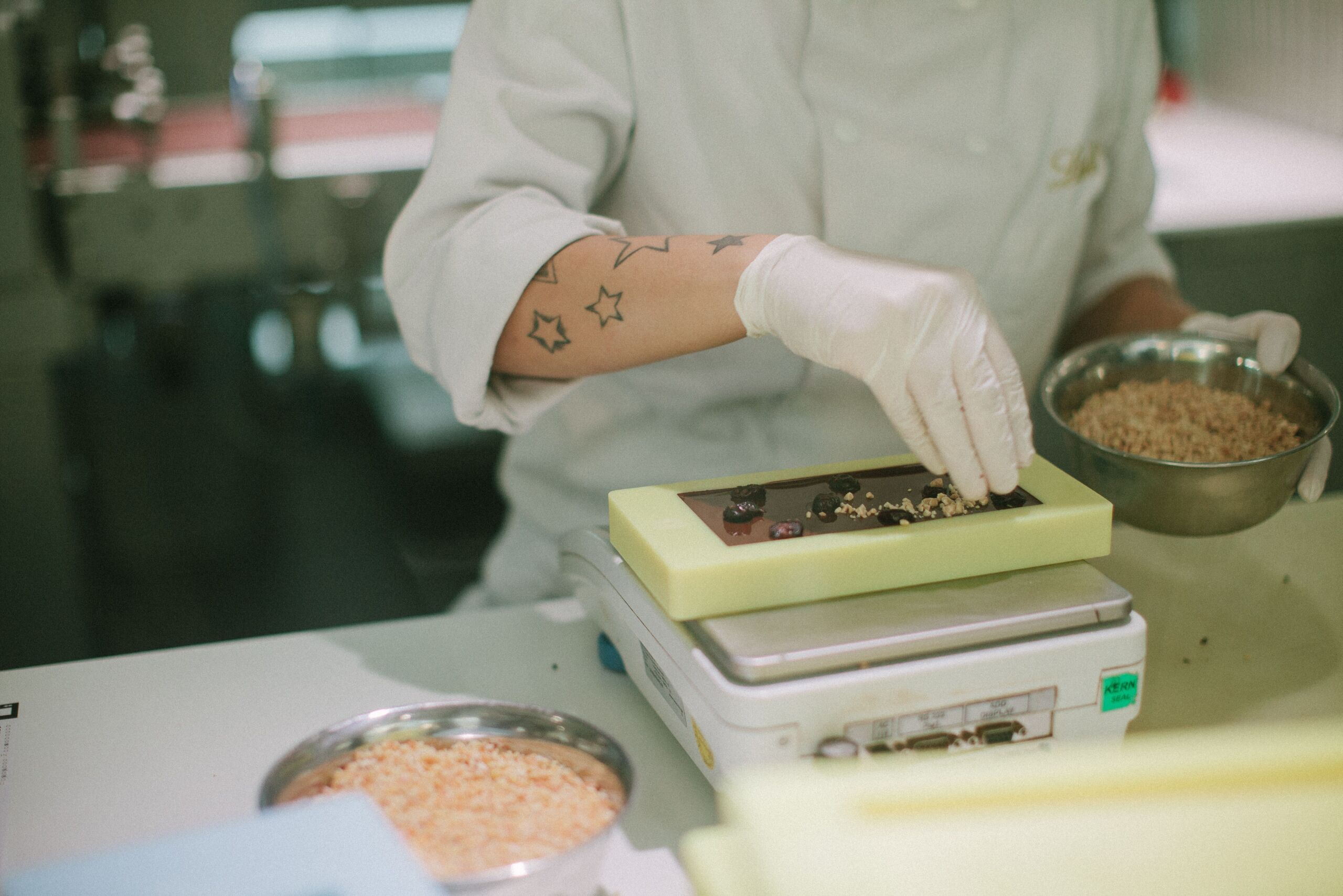 Close-up of a chocolatier adding toppings to a chocolate bar in a confectionery kitchen.